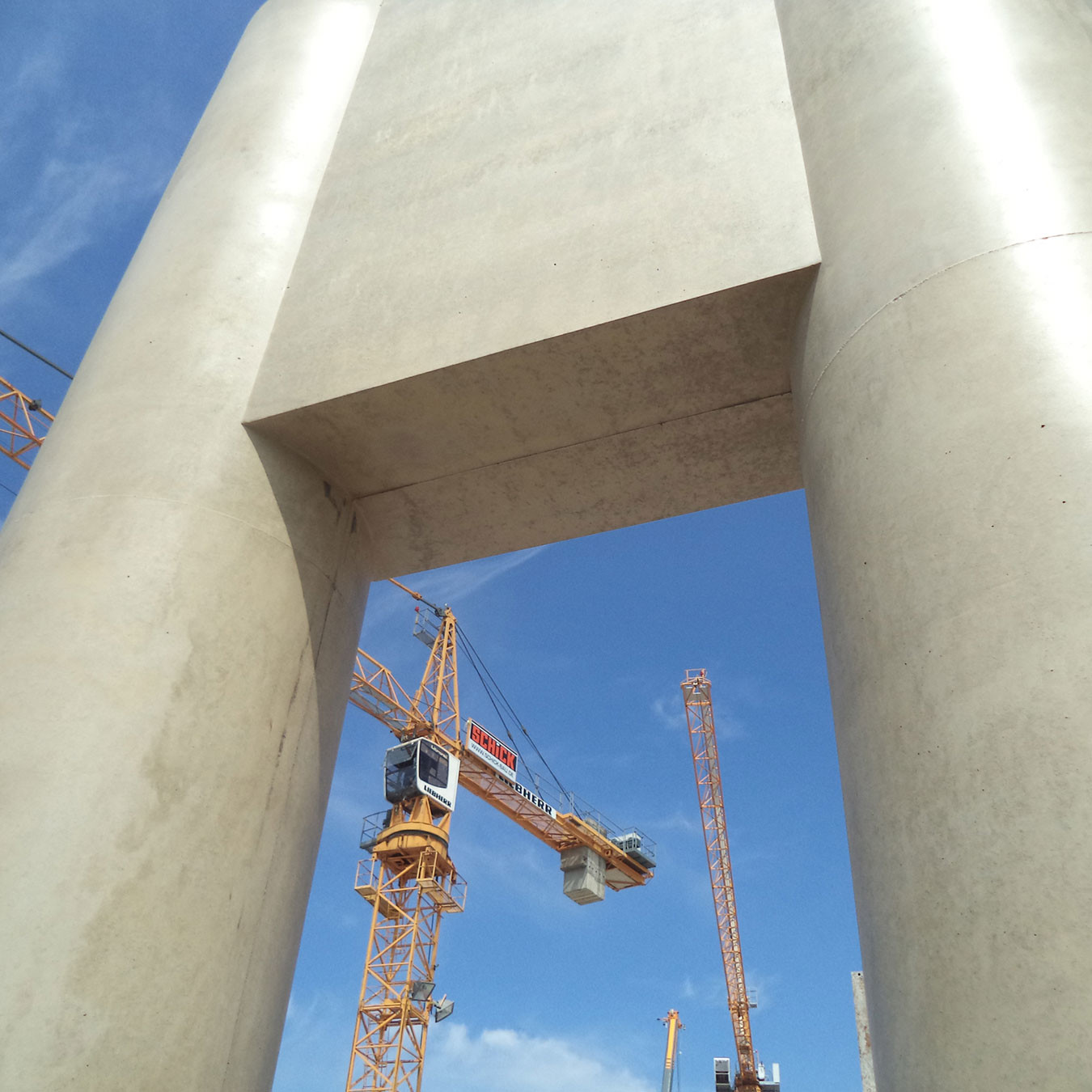 Looking up at two circular concrete columns with a crane in the background